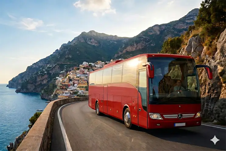 A red Mercedes luxury coach bus driving on the winding scenic highway of the Amalfi Coast with the vertical town of Positano in the background